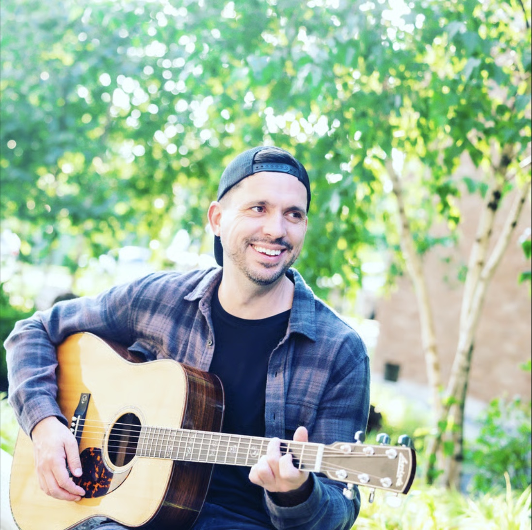 Eric Z smiling while playing acoustic guitar outdoors
