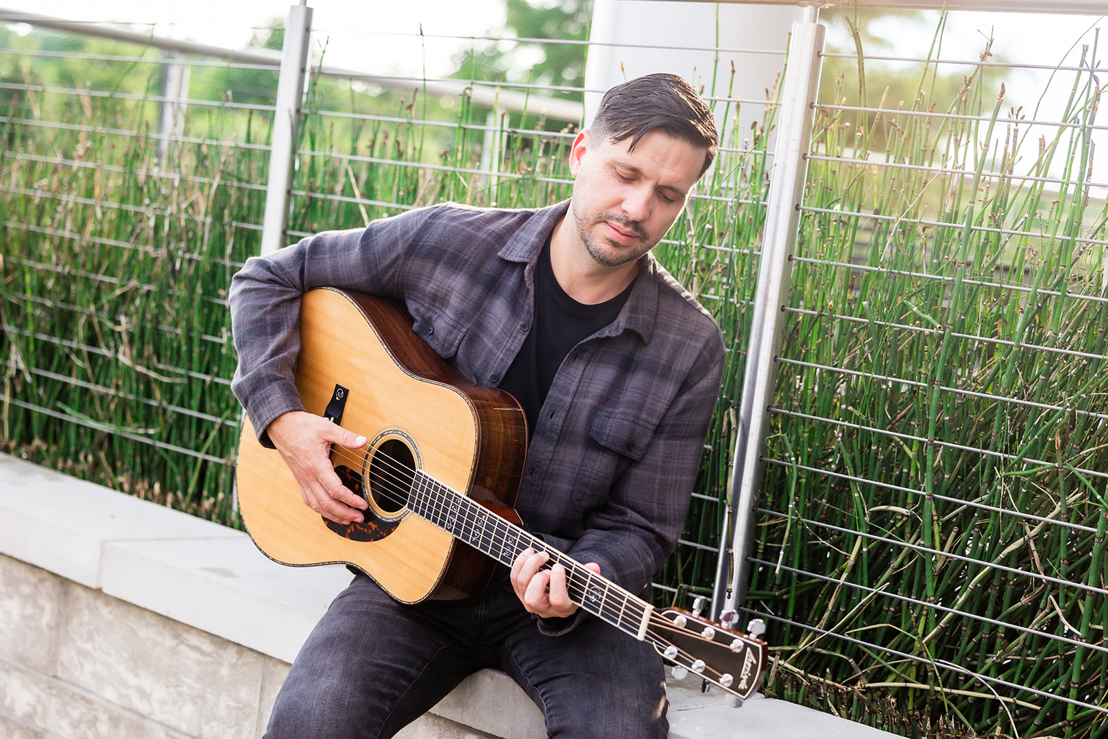 Eric Z sitting outdoors playing acoustic guitar